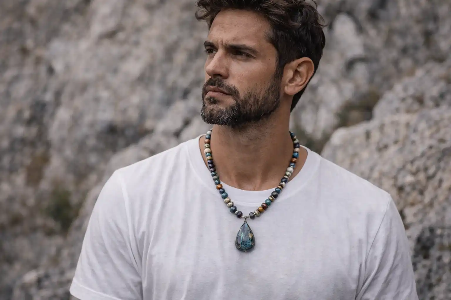 Homme portant un collier en pierre naturelle multicolore avec pendentif minéral devant des rochers naturels
