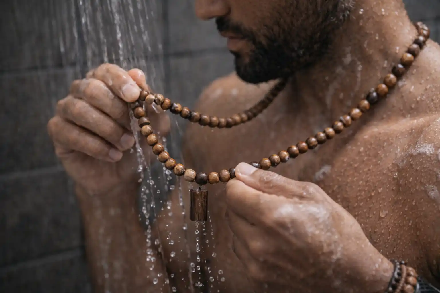 Homme sous la douche tenant un collier en bois mouillé avec perles naturelles exposées à l’eau